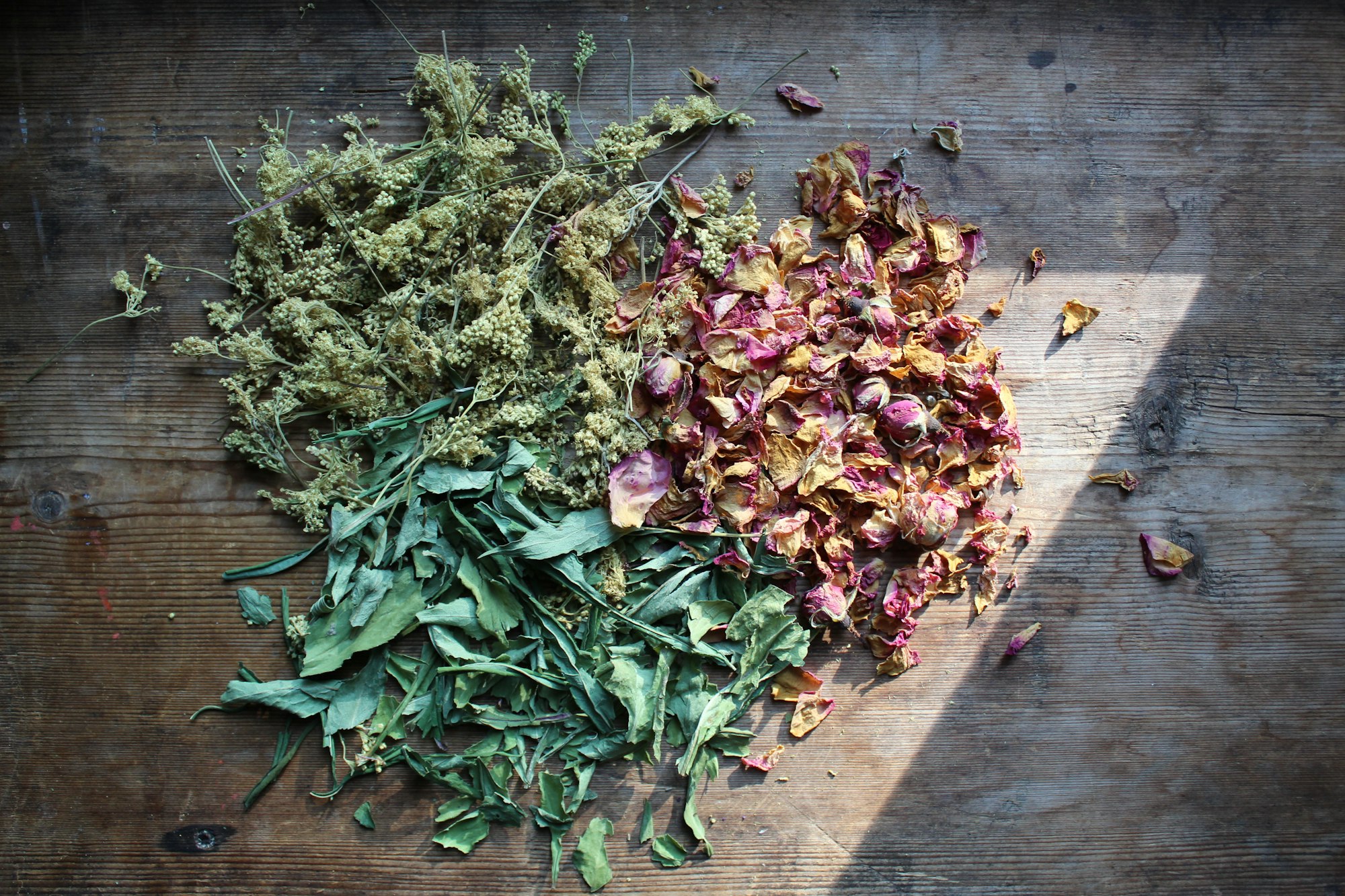 Dried herbs and rose petals spread across a weathered wooden table