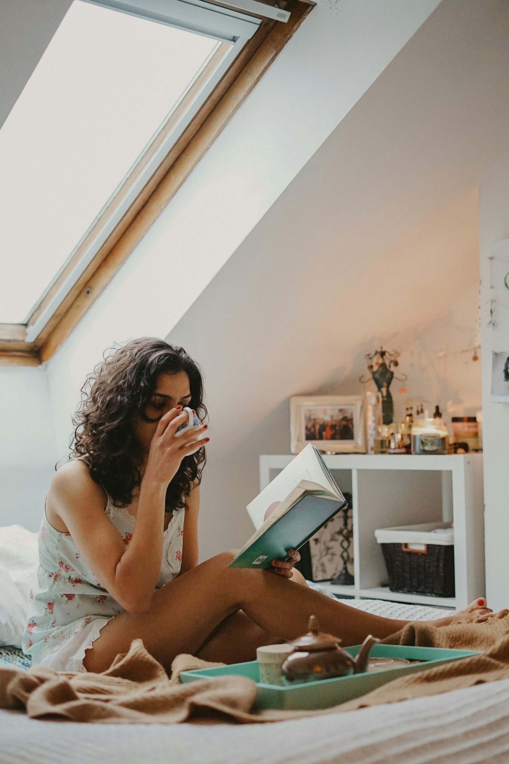 A woman drinking coffee and reading beside an attic window