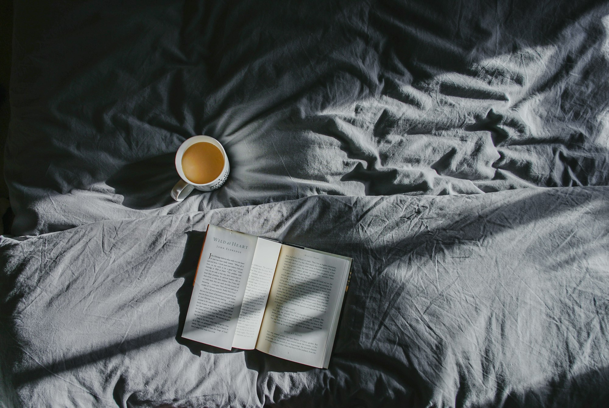 An open book and a white mug on soft grey bedding