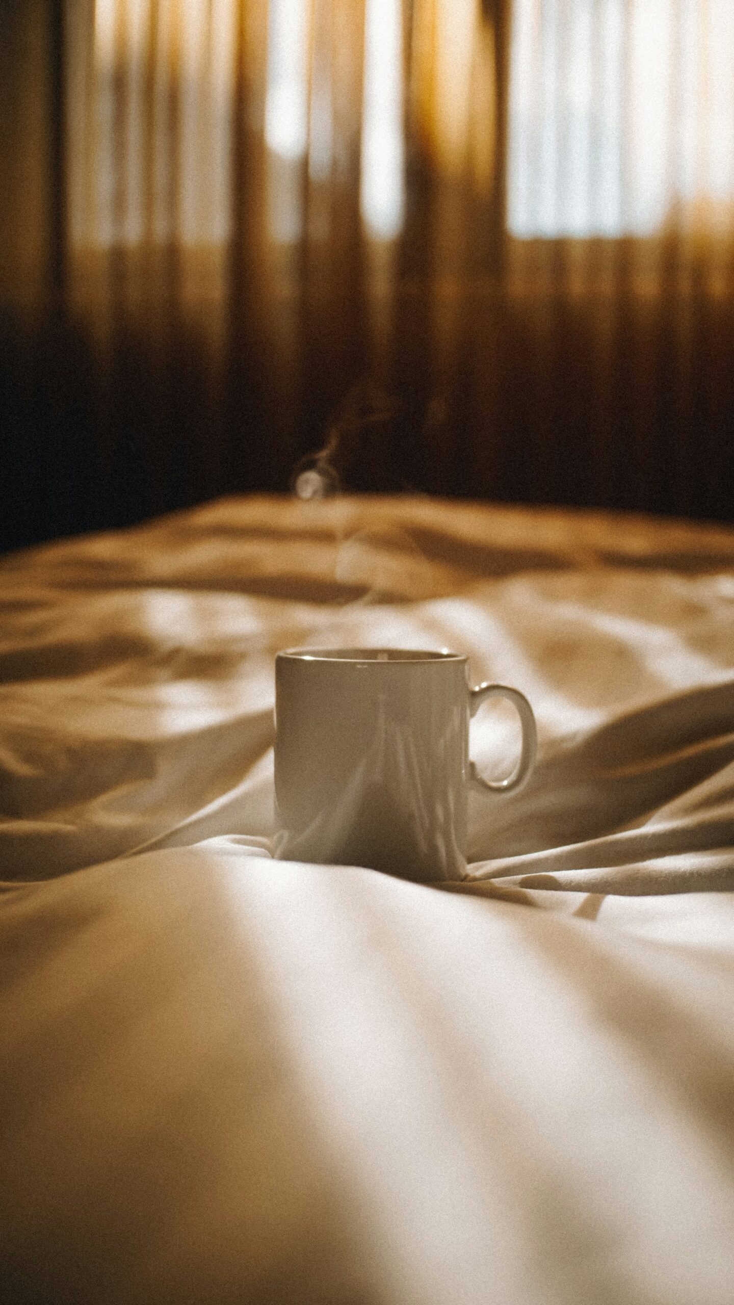 Steam rising from a pale mug set on golden-lit bedding
