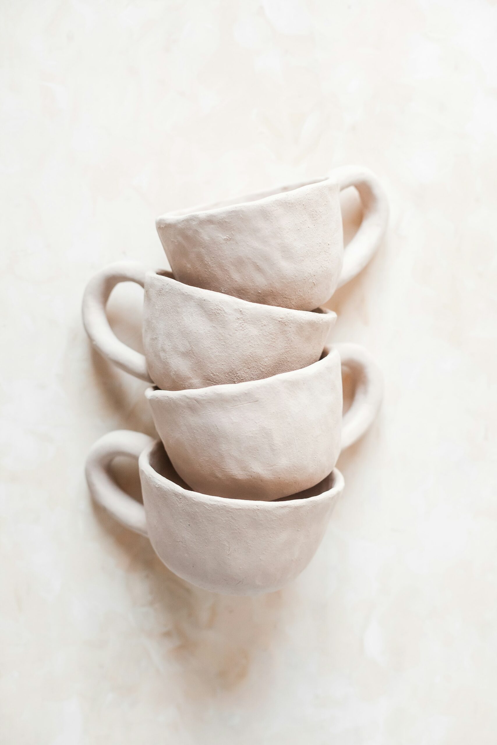 Four handmade ceramic cups stacked on a pale surface