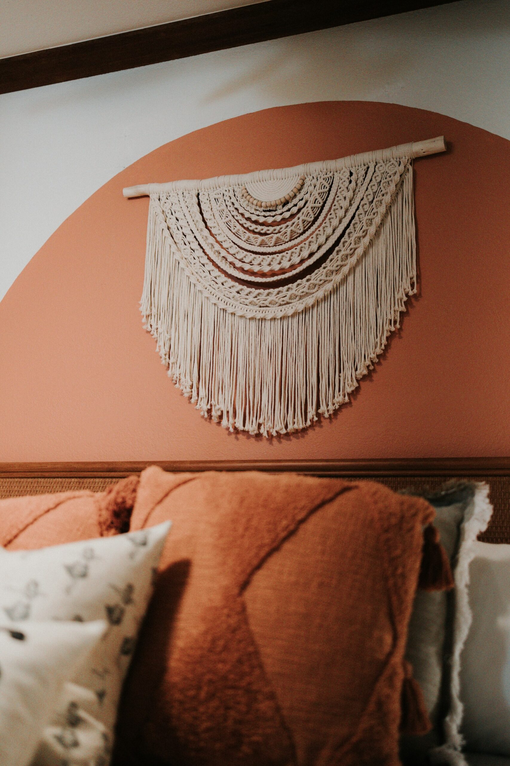 A macrame wall hanging above a bed against a warm terracotta wall
