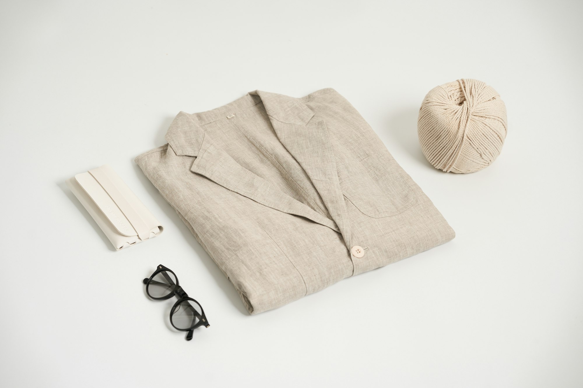 A folded linen shirt photographed from above with glasses and a ball of yarn