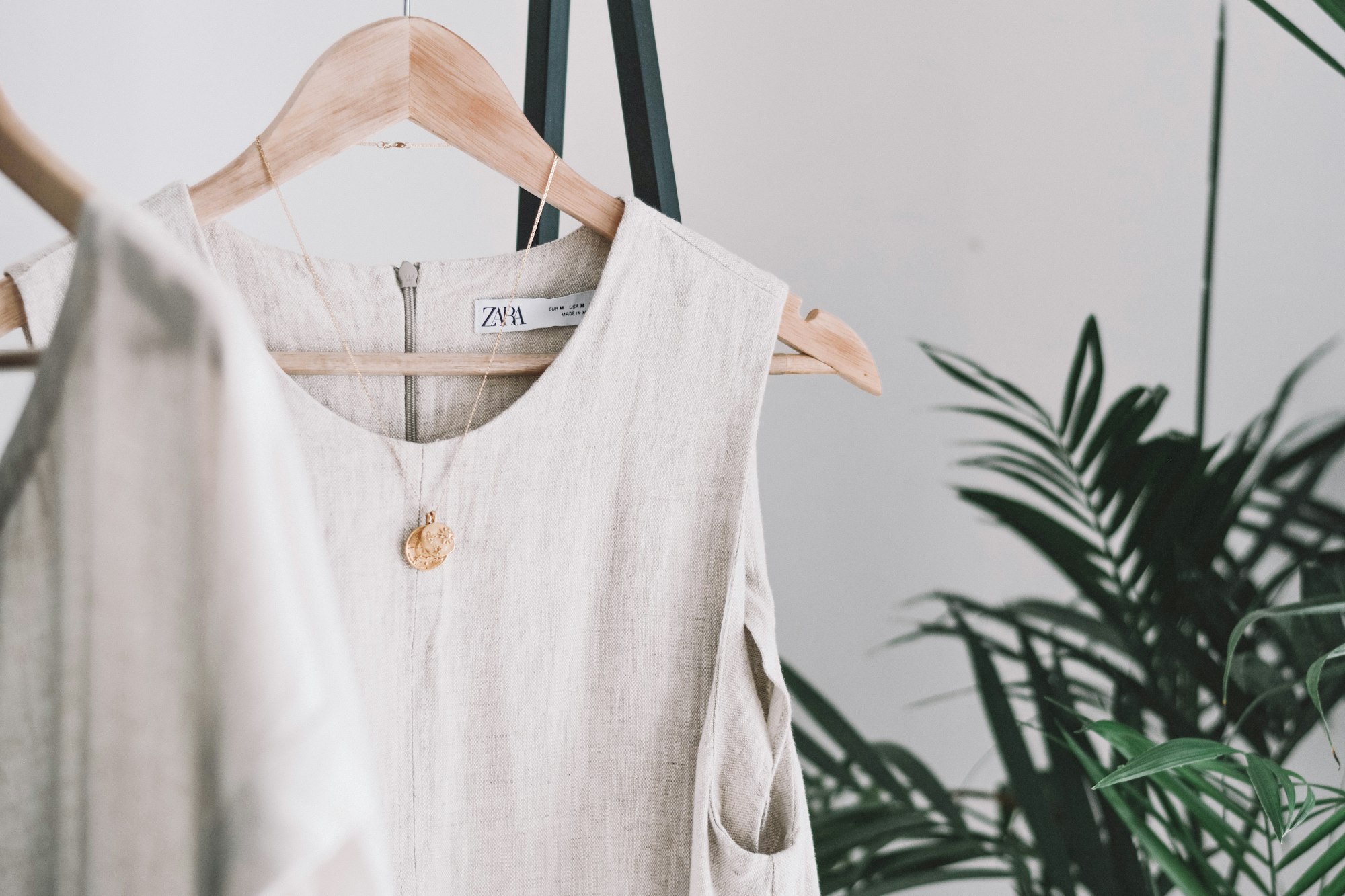 A sleeveless linen top on a wooden hanger against a pale wall