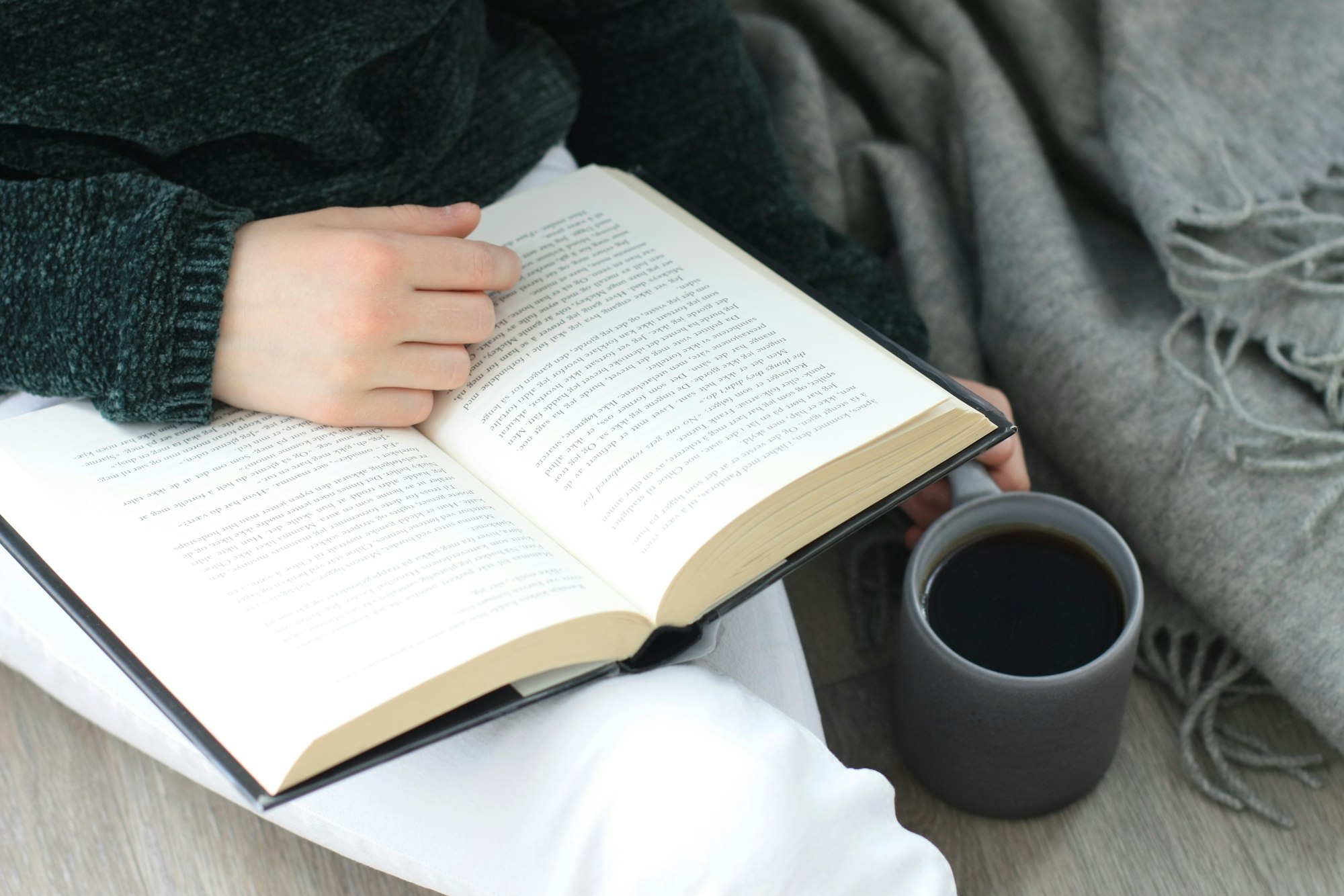 An open book and a cup of coffee held over a pale surface