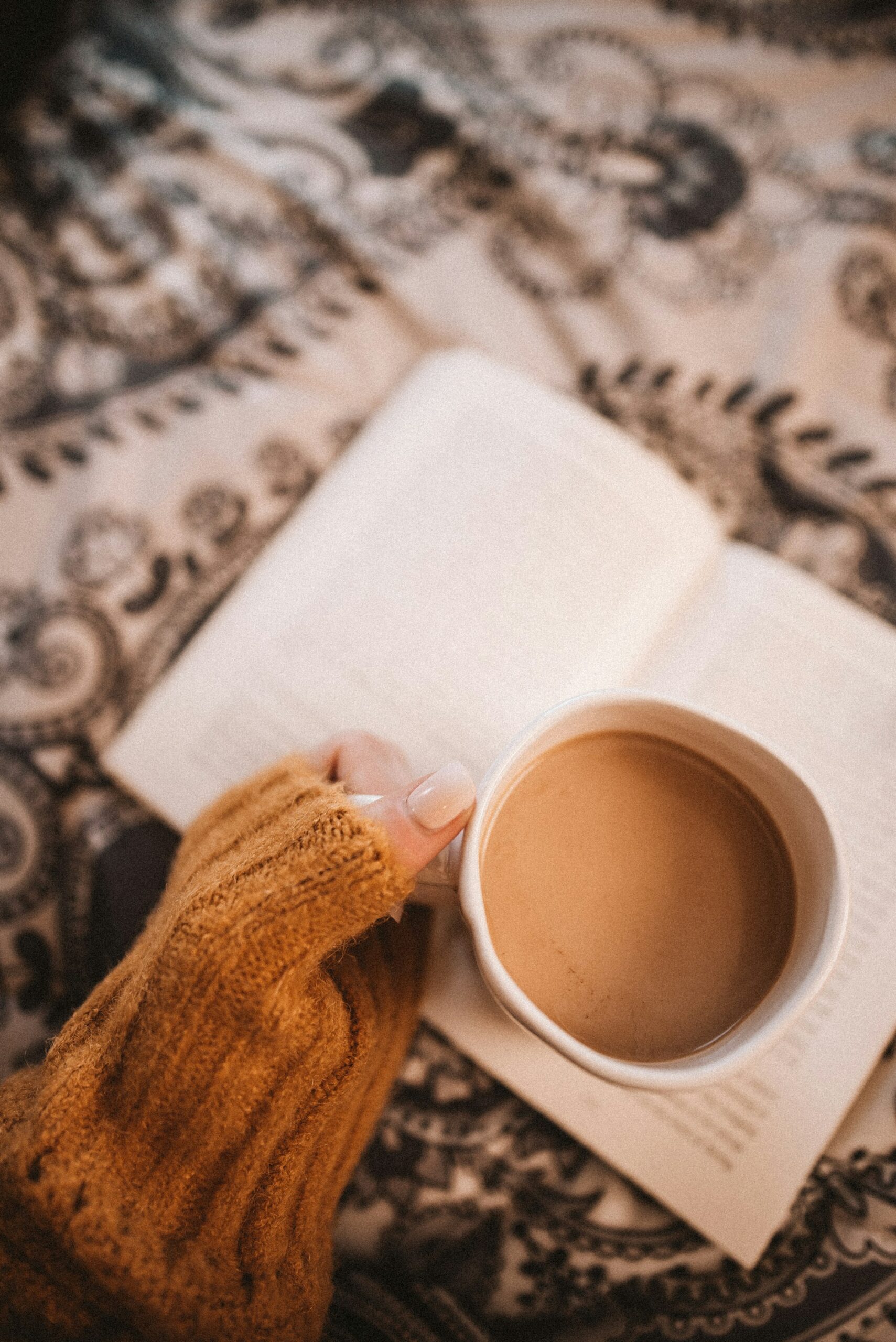Hands in a chunky knit sweater holding a mug of coffee