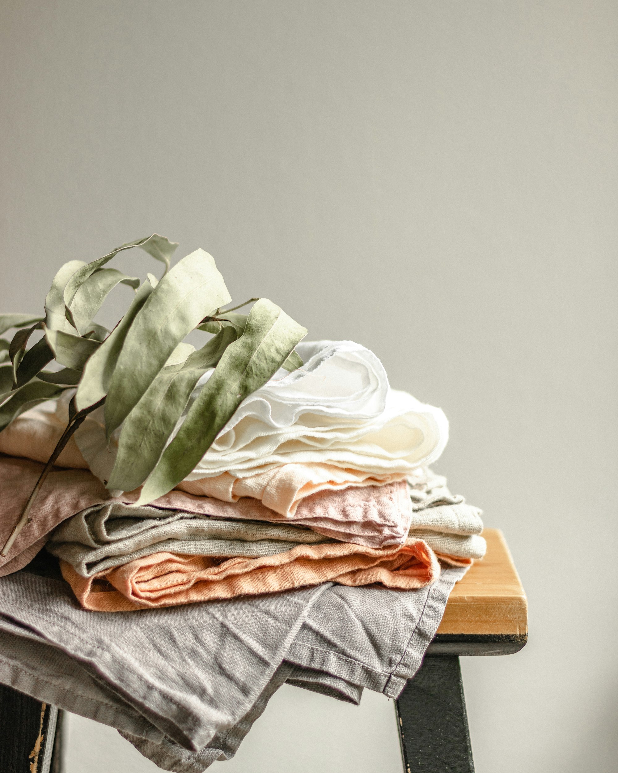 Folded sage and cream linen garments stacked on a wooden bench